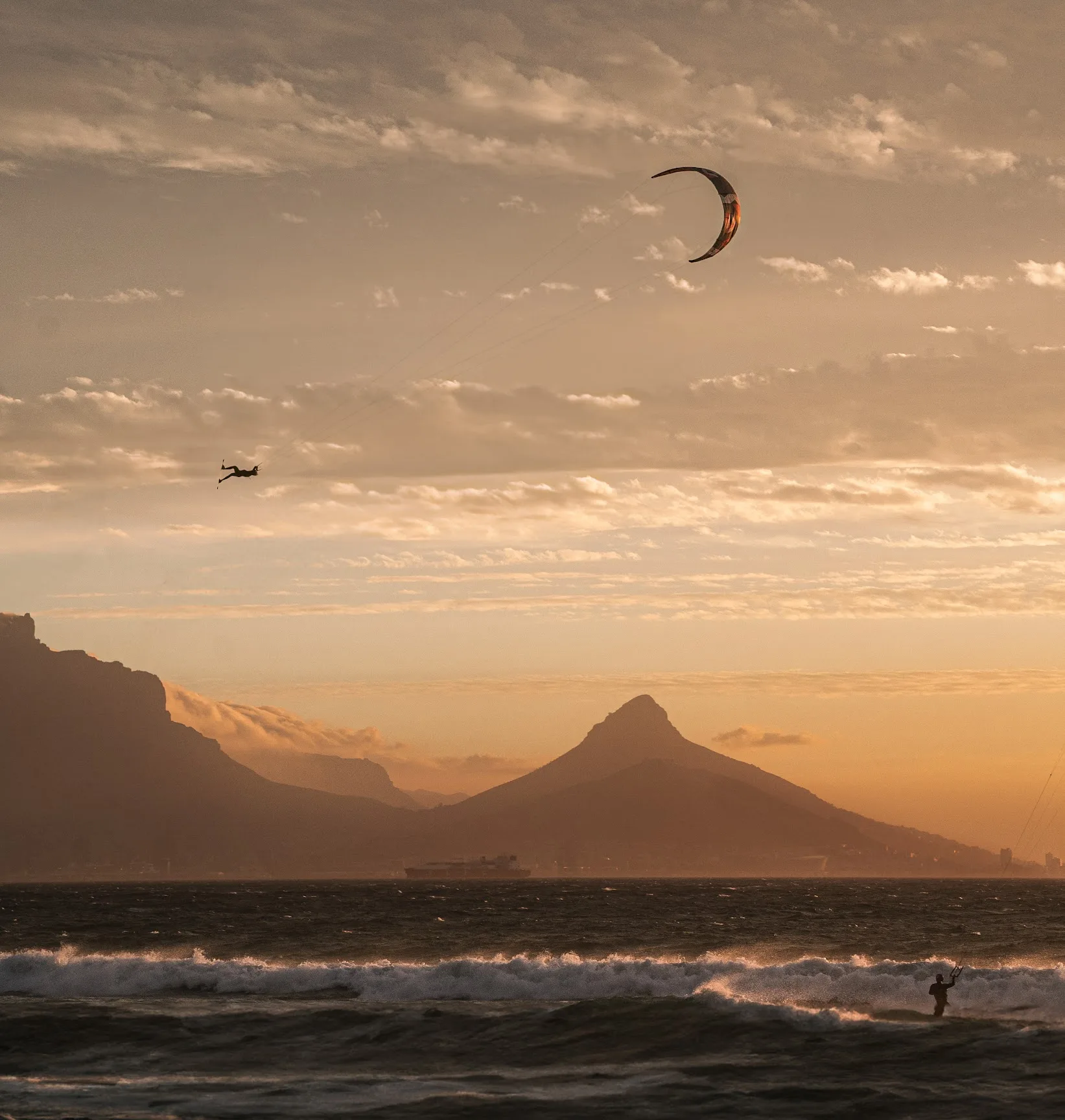 Kitesurfer flying high against an orange sunset sky above the ocean in Cape Town, with Table Mountain and Lion’s Head behind